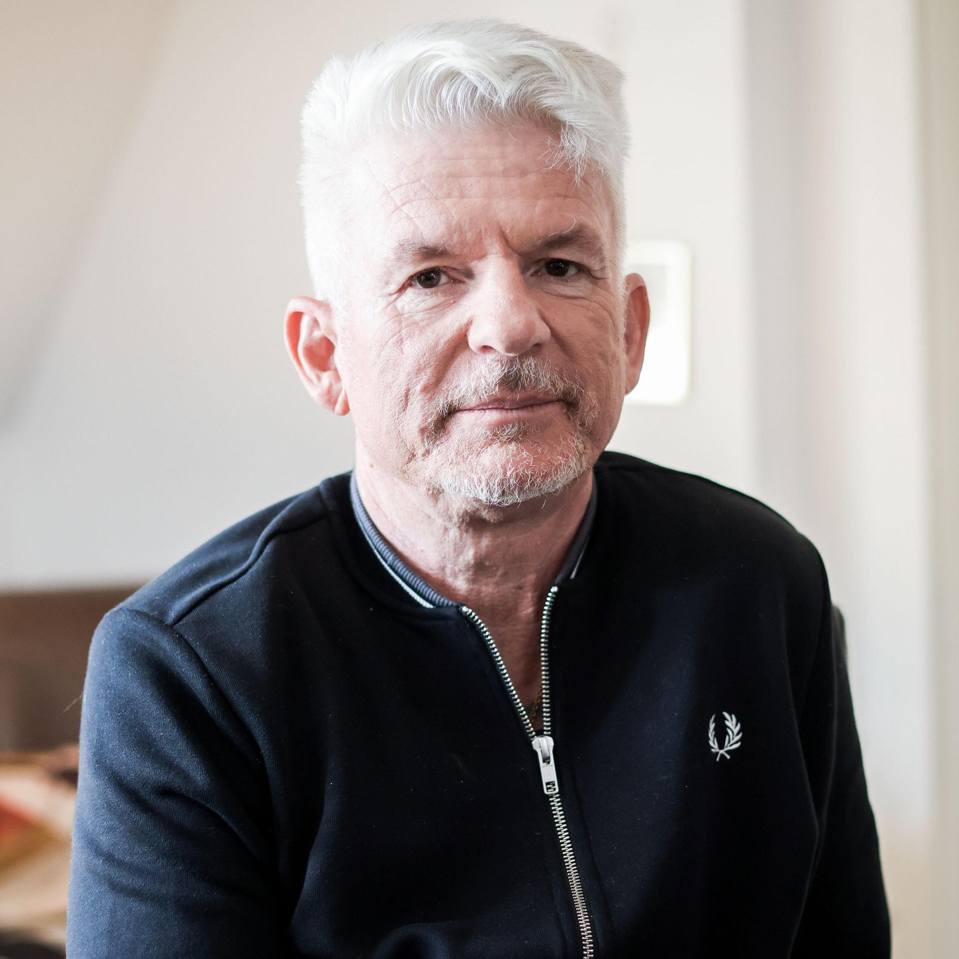 Heinz Strunk blickt in einer lichten Wohnung ernst in die Kamera