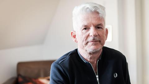 Heinz Strunk blickt in einer lichten Wohnung ernst in die Kamera