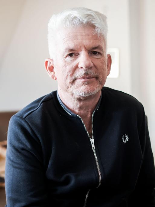 Heinz Strunk blickt in einer lichten Wohnung ernst in die Kamera