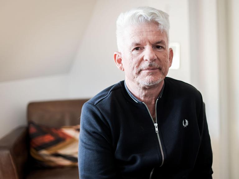 Heinz Strunk blickt in einer lichten Wohnung ernst in die Kamera