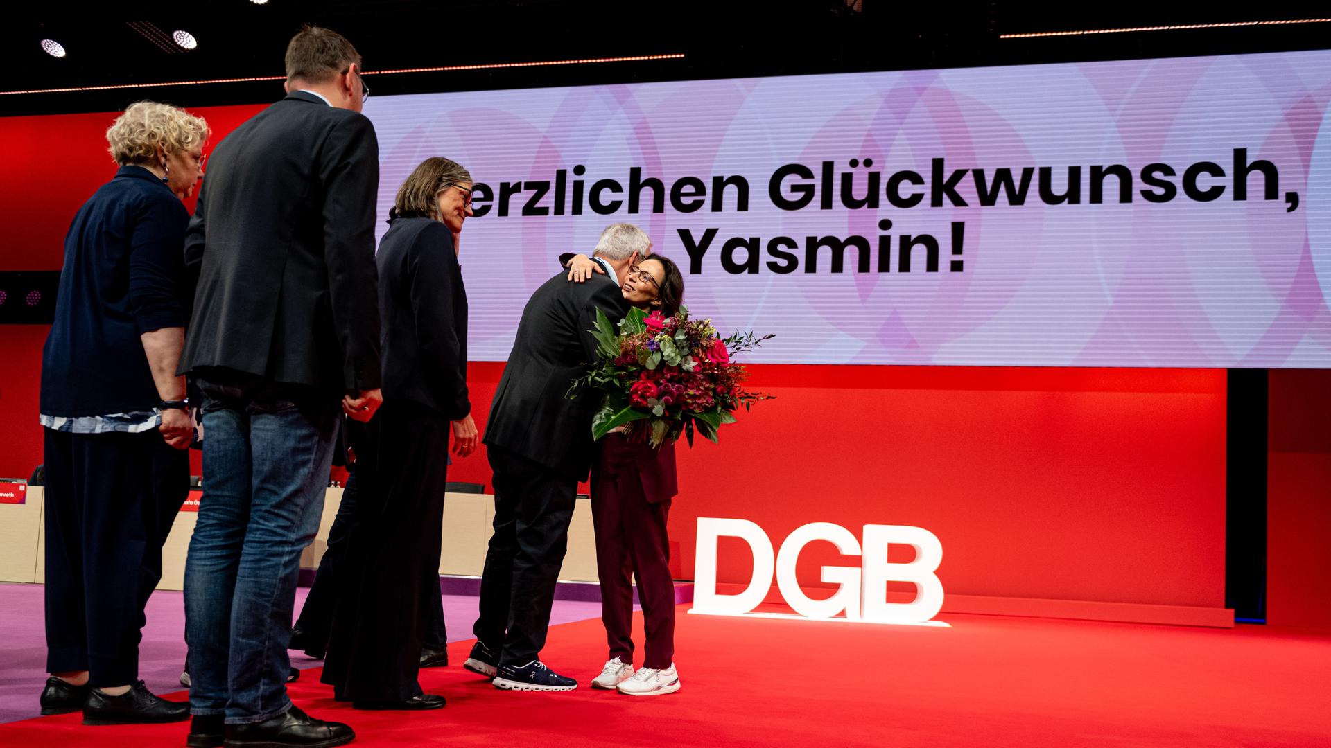 Yasmin Fahimi, DGB-Chefin, steht nach ihrer Wahl am Ordentlichen Bundeskongress des Deutschen Gewerkschaftsbundes (DGB) auf der Bühne und wird von mehreren Personen beglückwünscht. Yasmin Fahimi, DGB-Chefin, steht nach ihrer Wahl am Ordentlichen Bundeskongress des Deutschen Gewerkschaftsbundes (DGB) auf der Bühne und wird von mehreren Personen beglückwünscht.