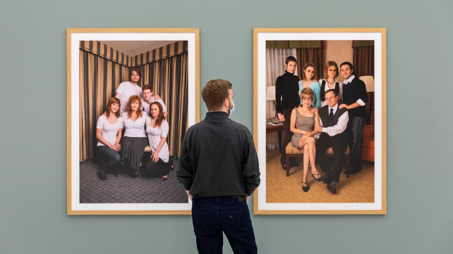 Ein Mann steht in einer Ausstellung vor zwei Fotografien, die jeweils eine Familie porträtieren.