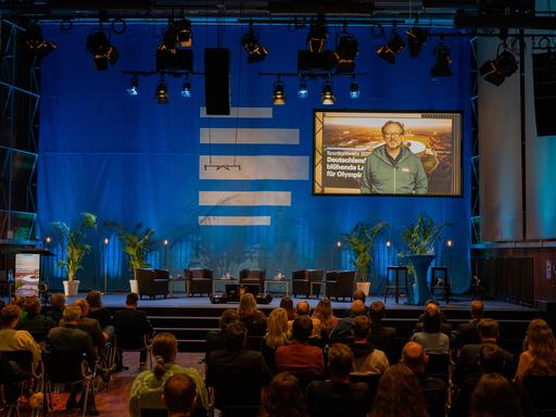 Bei der 10. Sportkonferenz im Deutschlandfunk ist der Impulsvortrag von Eckart von Hirschhausen auf der Leinwand zu sehen.