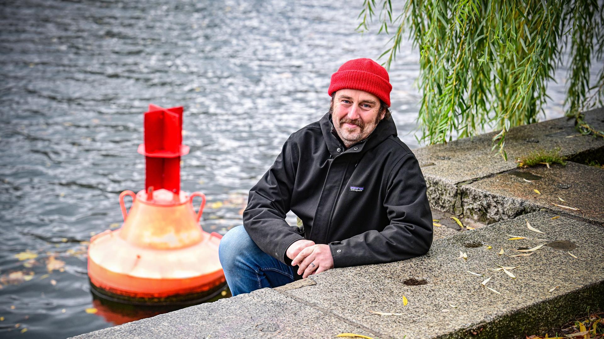 Ein Mann mit einer Mütze auf dem Kopf sitzt an einem Kanal in Berlin Ein Mann mit einer Mütze auf dem Kopf sitzt an einem Kanal in Berlin