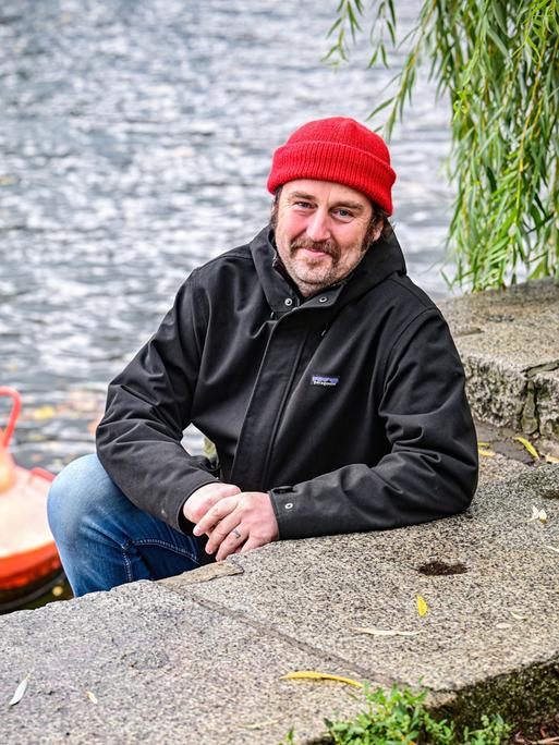 Ein Mann mit einer Mütze auf dem Kopf sitzt an einem Kanal in Berlin