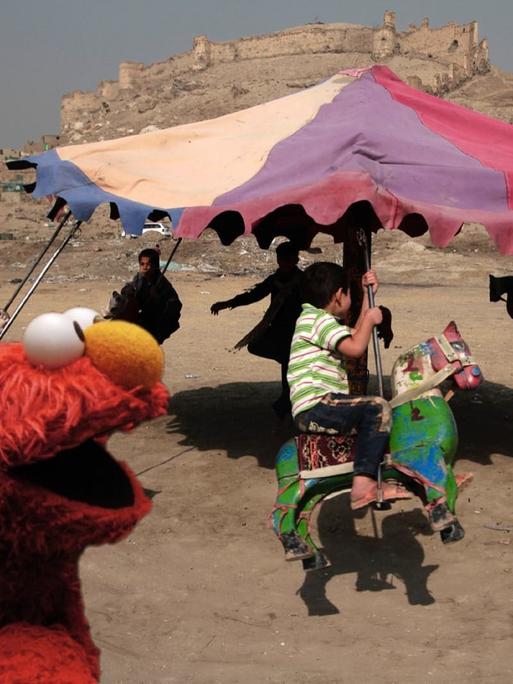 Elmo vor einem Karussell, mit dem afghanische Kinder in der Nähe von Kabul fahren