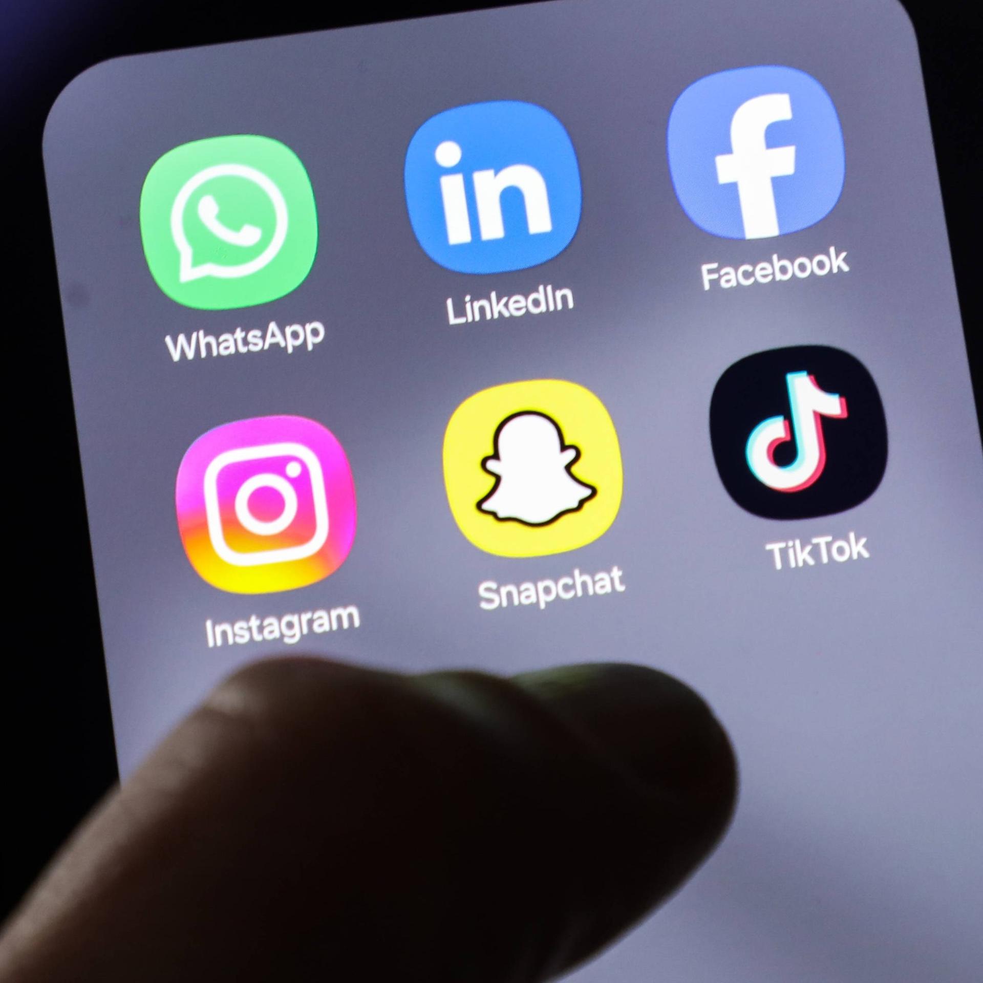 Auf einem Handybildschirm sind verschiedene Apps für Social-Media-Plattformen wie Instagram, Facebook oder Tiktok sichtbar. Über dem Bildschirm schwebt eine Hand. Auf einem Handybildschirm sind verschiedene Apps für Social-Media-Plattformen wie Instagram, Facebook oder Tiktok sichtbar. Über dem Bildschirm schwebt eine Hand.
