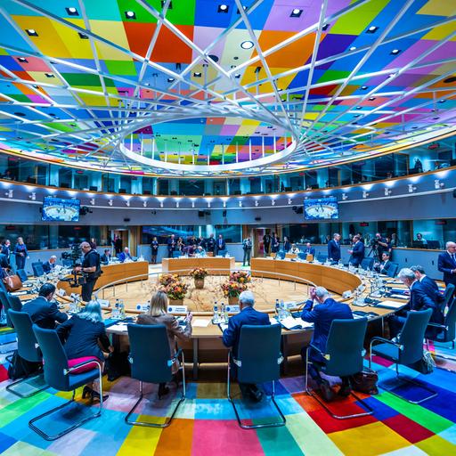 Die Staats- und Regierungschefs der EU-Staaten beraten an einem runden Tisch in Brüssel. Er steht auf einem bunten Teppich, der sich in der Decke spiegelt. 