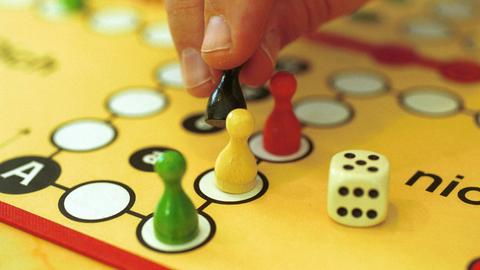 Nahaufnahme einer Hand, die Spielsteine bei einem Mensch-Ärgere-Dich-Nicht-Spiel bewegt.