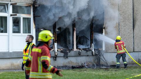 Feuerwehrleute löschen einen Brand in einer Flüchtlingsunterkunft in Apolda. Aus geborstenen Fernstern steigt dichter Rauch auf.