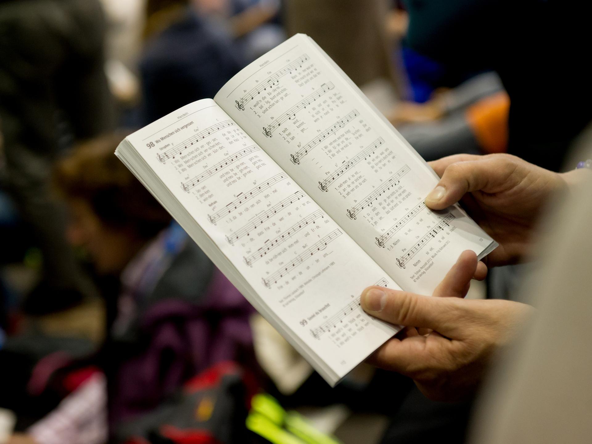Ein Kirchenbesucher hält ein Gesangsbuch in den Händen, während im Hintergrund bunte Flecken auftauchen.