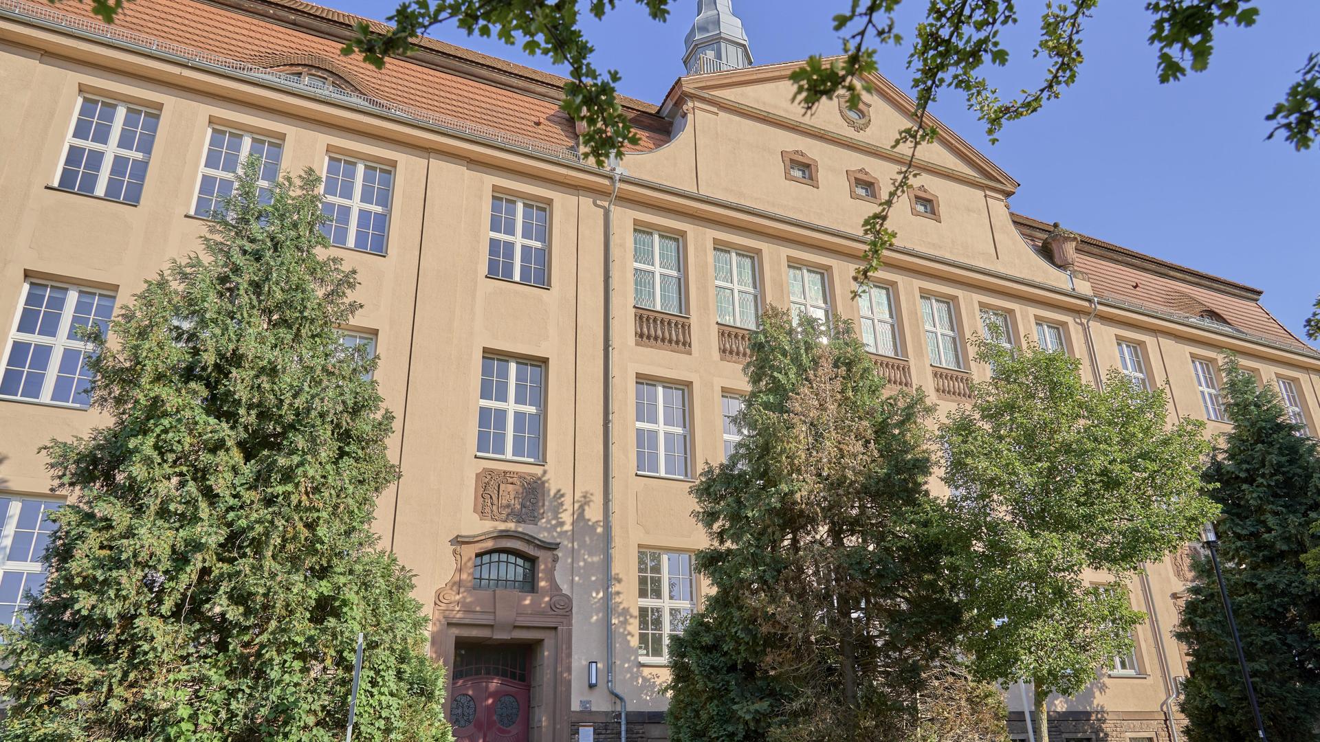 Fassade eines großen, historischen Schulgebäudes mit umliegenden Bäumen Fassade eines großen, historischen Schulgebäudes mit umliegenden Bäumen