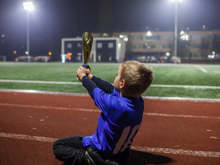 Junger Fußballspieler in blauem Jersey hält den Pokal in die Luft in einem Stadium