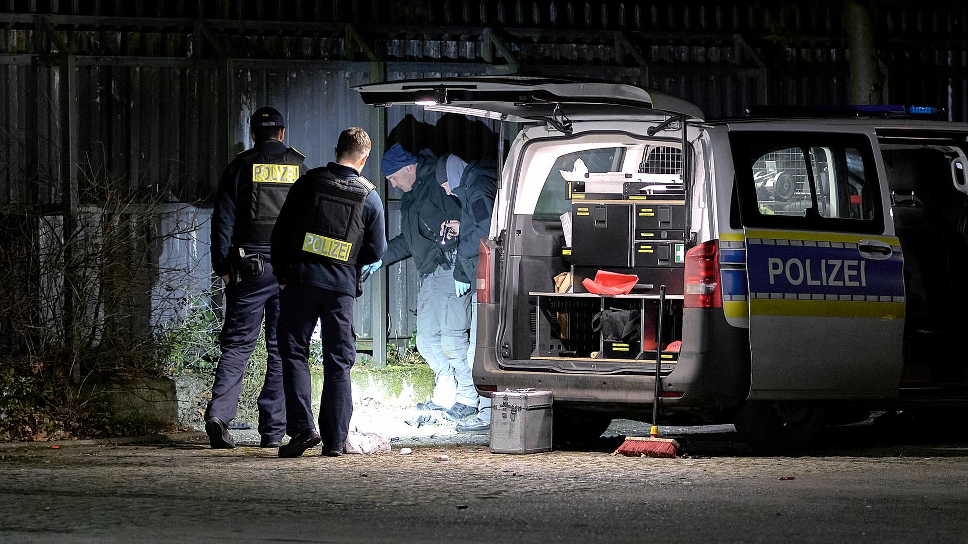 Einsatzkräfte der Polizei ermitteln bei Dunkelheit an einem Tatort. Zu sehen ist auch ein großes Einsatzfahrzeug mit einer geöffneten Hintertür und einer mit Material vollgepackten Ladefläche. 