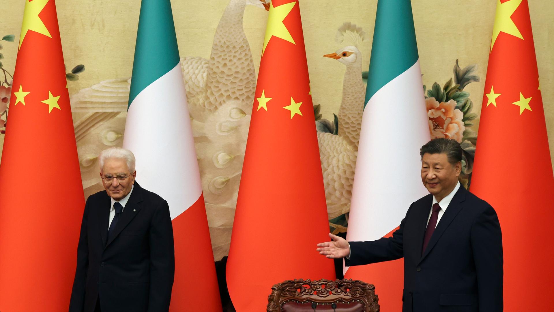 Xi Jinping und Mattarella stehen hinter Tischen, hinter ihnen die Landesfahnen. Xi Jinping und Mattarella stehen hinter Tischen, hinter ihnen die Landesfahnen.