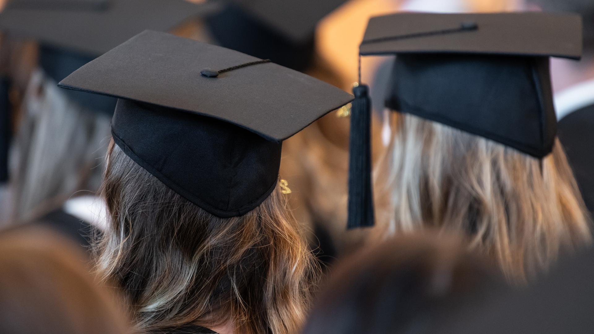 Absolventinnen der Universität Mannheim tragen während der Abschlussfeier in der Aula Absolventenhüte.