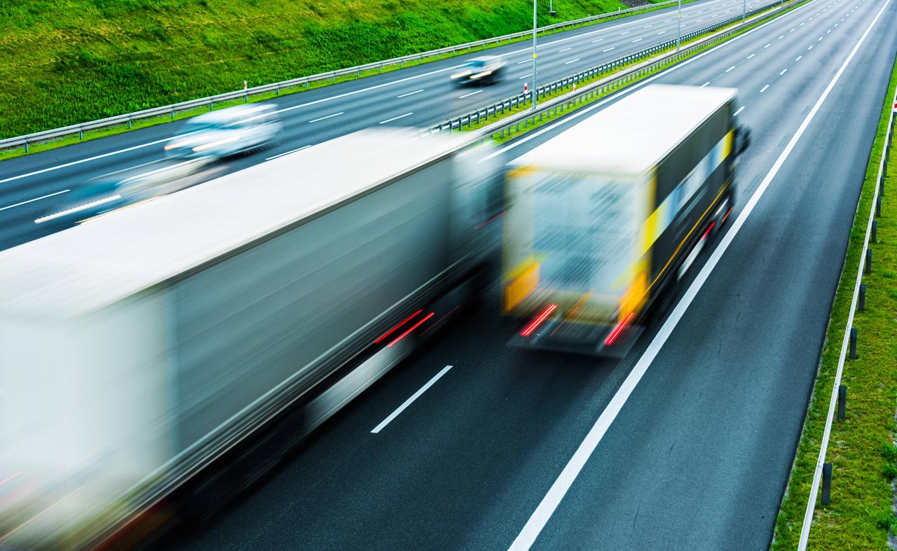 Im Vordergrund fahren auf einer Autobahn zwei LKW. Im Hintergrund sind noch zwei Autos erkennbar.