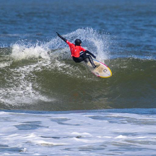 Auf dem Bild ist ein Surfer zu sehen, der über eine Welle reitet. 
