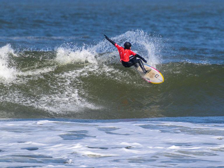 Auf dem Bild ist ein Surfer zu sehen, der über eine Welle reitet. 