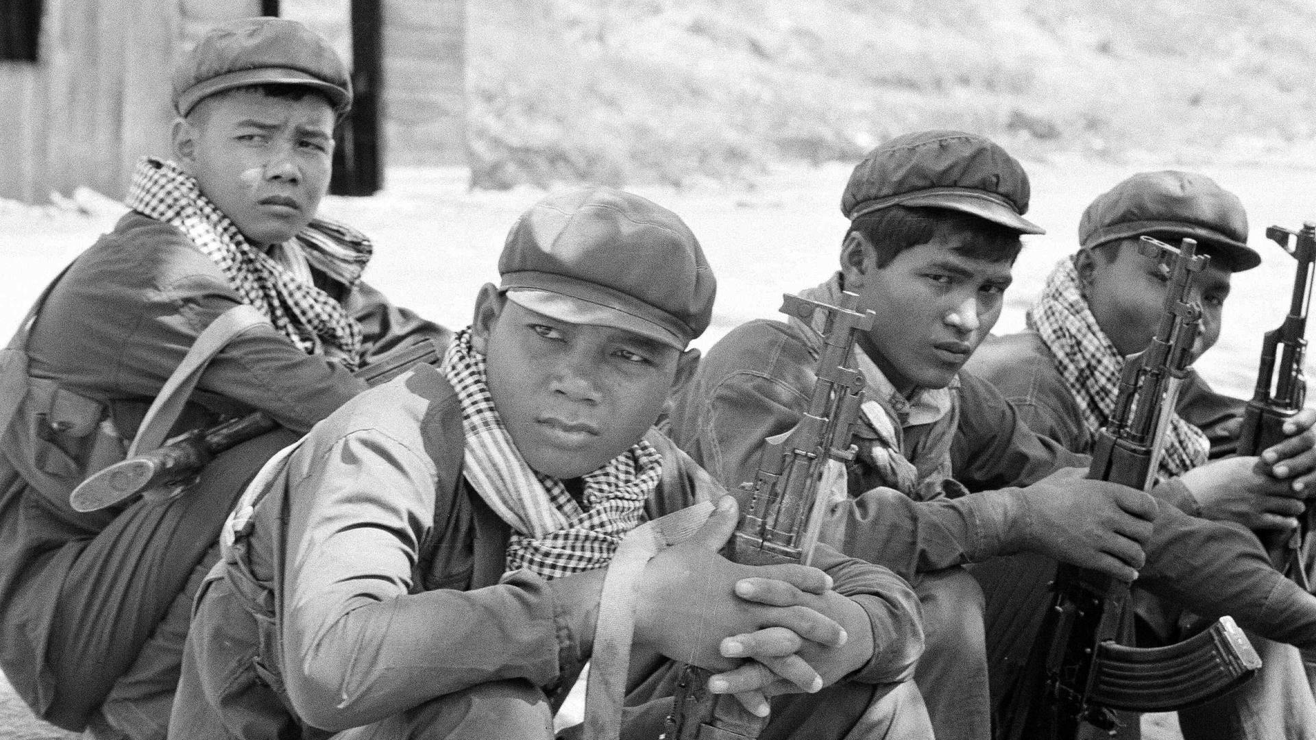 Historisches Schwarzweißfoto von Soldaten der Roten Khmer mit charakteristischen Schals, die mit ihren Waffen in einer Gruppe auf dem Boden sitzen. Historisches Schwarzweißfoto von Soldaten der Roten Khmer mit charakteristischen Schals, die mit ihren Waffen in einer Gruppe auf dem Boden sitzen.