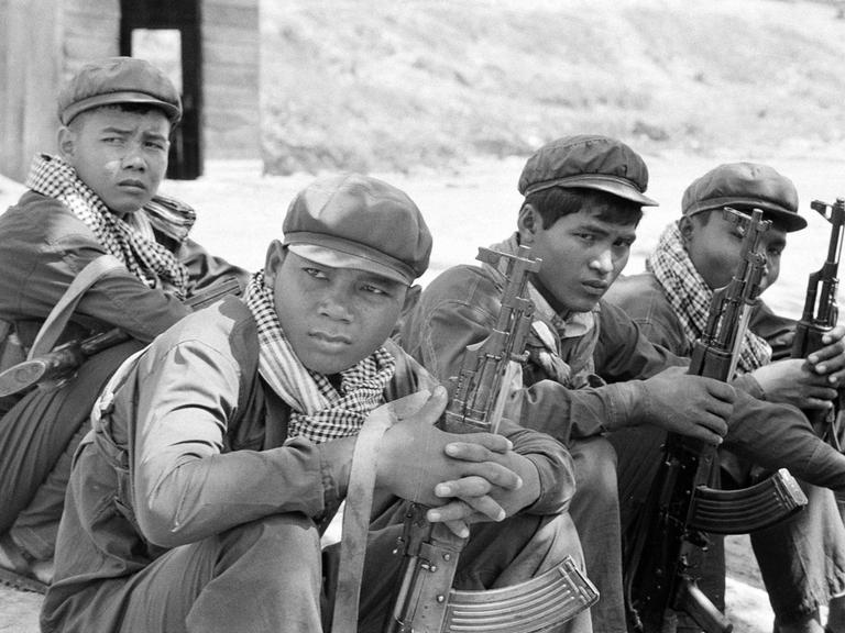 Historisches Schwarzweißfoto von Soldaten der Roten Khmer mit charakteristischen Schals, die mit ihren Waffen in einer Gruppe auf dem Boden sitzen.
