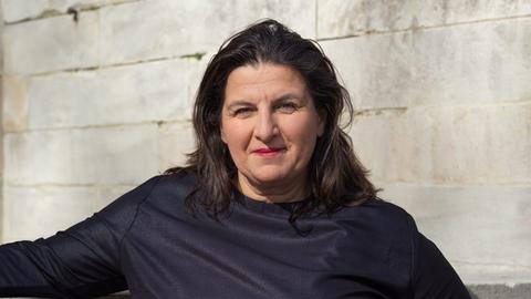 Porträt von Çağla Ilk. Eine Frau mittleren Alters mit dunkelbraunem schulterlangen Haar in einem schwarzen Kleid.