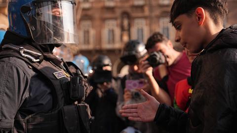 Ein Schüler steht gegenüber einem Polizisten in Kampfmontur inklusive Helm. Der Junge reicht dem Beamten die Hand.