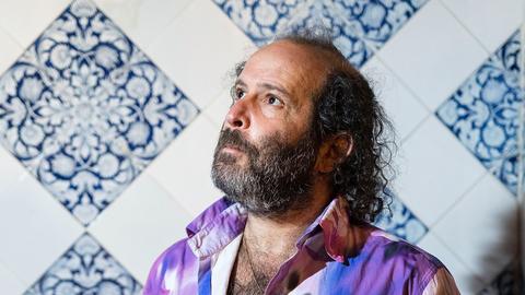 Tomer Gardi bei der Veranstaltung zur Vorstellung seines Buches im Literarischen Colloquium Berlin. Er steht vor in einem bunten Hemd vor einer gekachelten Wand und schaut in linke obere Bildecke.