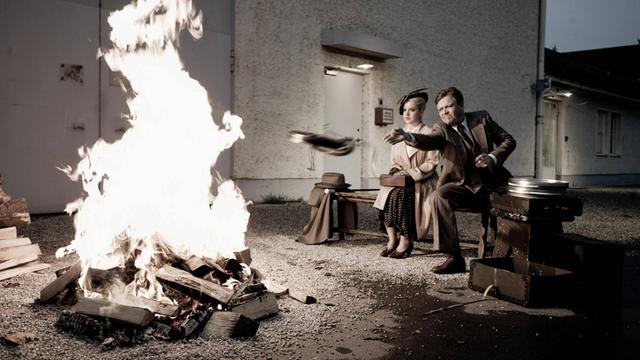 Filmszene aus "Jud Süß - Film ohne Gewissen", bei der zwei Darstellende neben einem Feuer sitzen und ein Buch verbrennen.