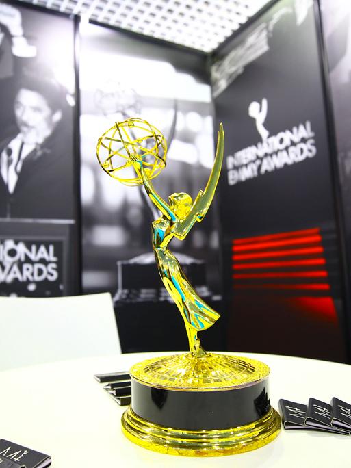 Die Trophäe des International Emmy Awards steht auf einem Tisch. Im Hintergrund sind schwarz-weiße Poster und auch der Schriftzug "Internationl Emmy Awards" zu sehen. Die Trophäe des International Emmy Awards steht auf einem Tisch. Im Hintergrund sind schwarz-weiße Poster und auch der Schriftzug "Internationl Emmy Awards" zu sehen.