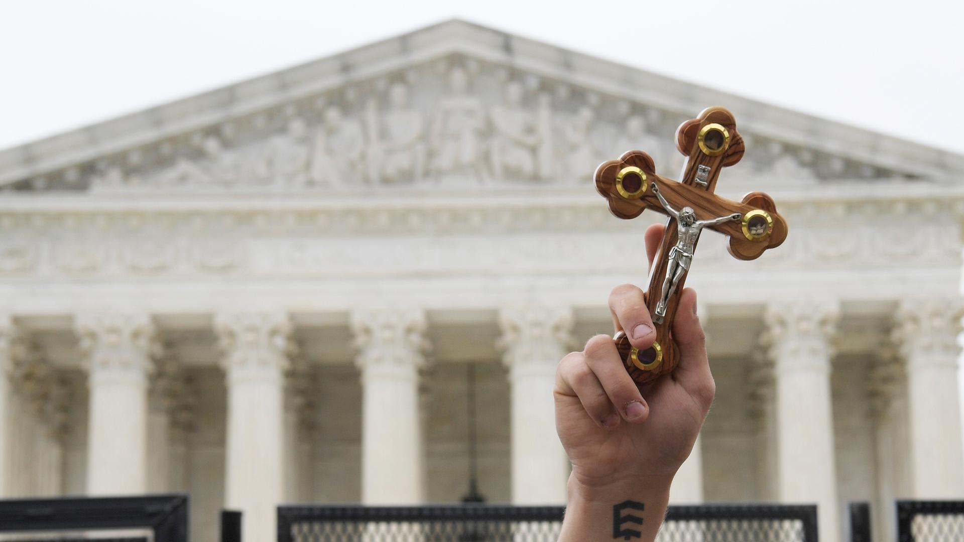 Ein Demonstrant hält ein Kreuz in die Luft. Im Hintergrund: der Supreme Court.