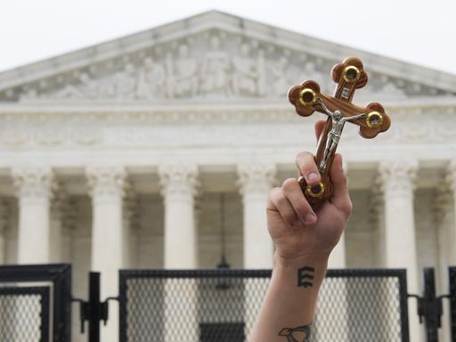 Ein Demonstrant hält ein Kreuz in die Luft. Im Hintergrund: der Supreme Court.