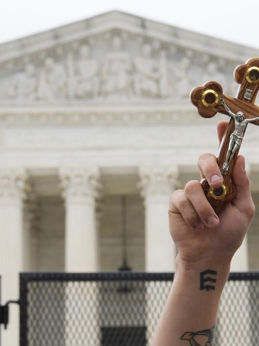 Ein Demonstrant hält ein Kreuz in die Luft. Im Hintergrund: der Supreme Court.