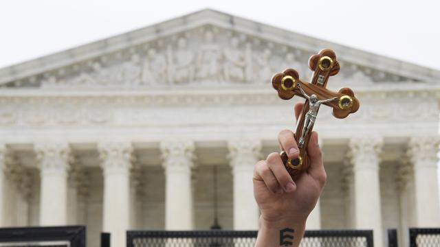 Ein Demonstrant hält ein Kreuz in die Luft. Im Hintergrund: der Supreme Court.