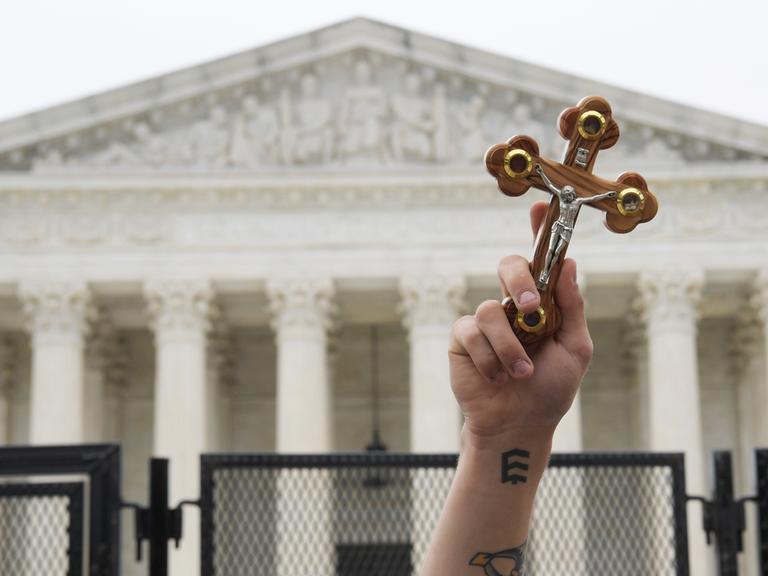 Ein Demonstrant hält ein Kreuz in die Luft. Im Hintergrund: der Supreme Court. Ein Demonstrant hält ein Kreuz in die Luft. Im Hintergrund: der Supreme Court.
