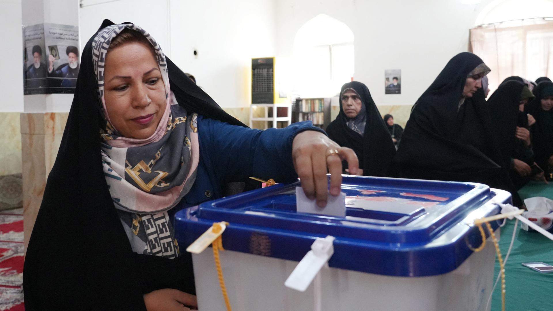 Eine Frau mit schwarzem Kopftuch wirft in Teheran ihren Stimmzettel in eine Wahlurne mit blauem Deckel. 