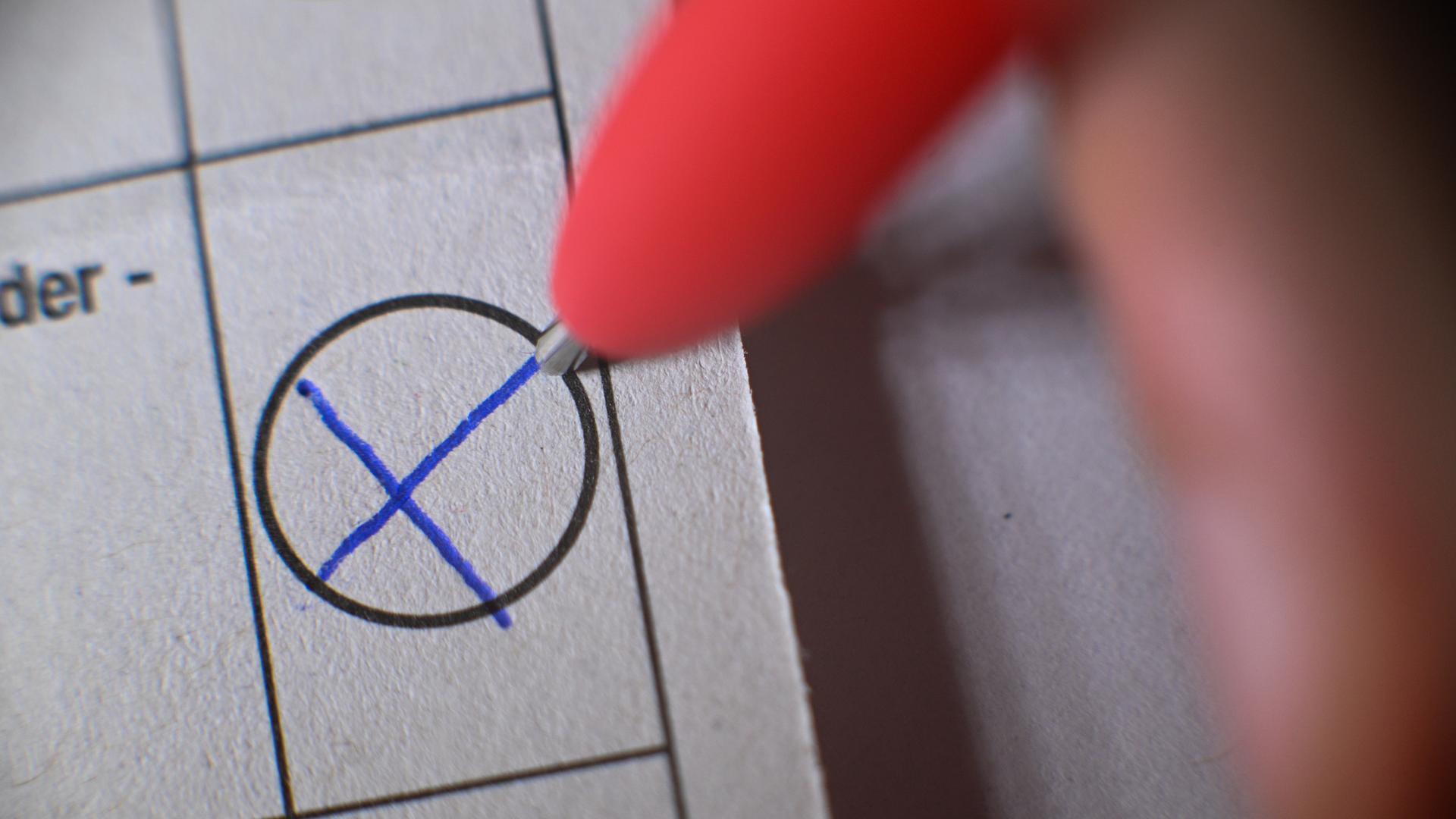 Eine Hand macht mit einem Kugelschreiber ein Kreuz auf einem Wahlzettel.