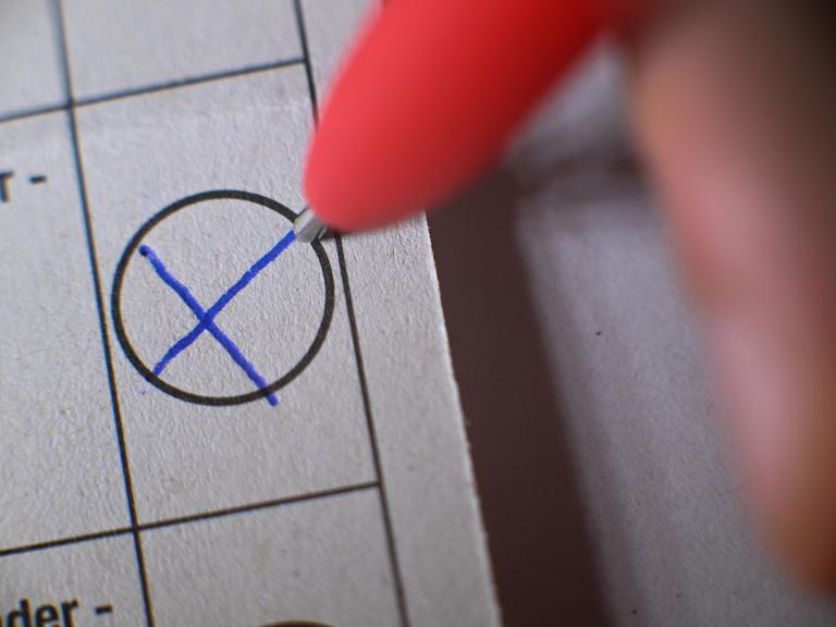 Eine Hand macht mit einem Kugelschreiber ein Kreuz auf einem Wahlzettel.