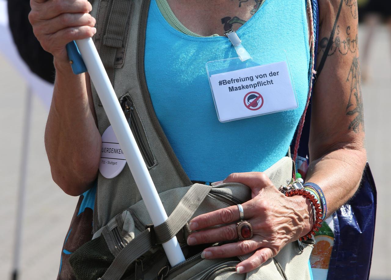 Eine Demonstrantin auf einer "Hygienedemo" in Berlin trägt ein Schild auf dem T-Shirt mit der Aufschrift "#Befreiung der Maskenpflicht" und ein "Querdenken"-Button an ihrem Rucksack. 