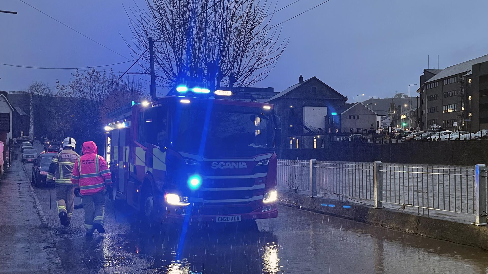 Das Foto zeigt ein Feuerwehrauto auf einer überfluteten Straße in Wales. 