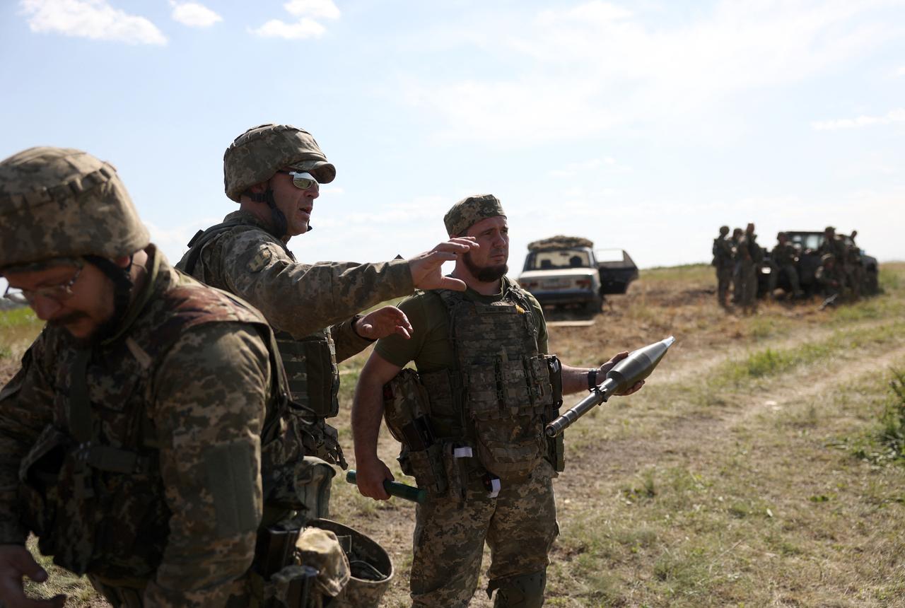 Ukrainische Soldaten stehen mit militärischem Gerät auf einem Feld.