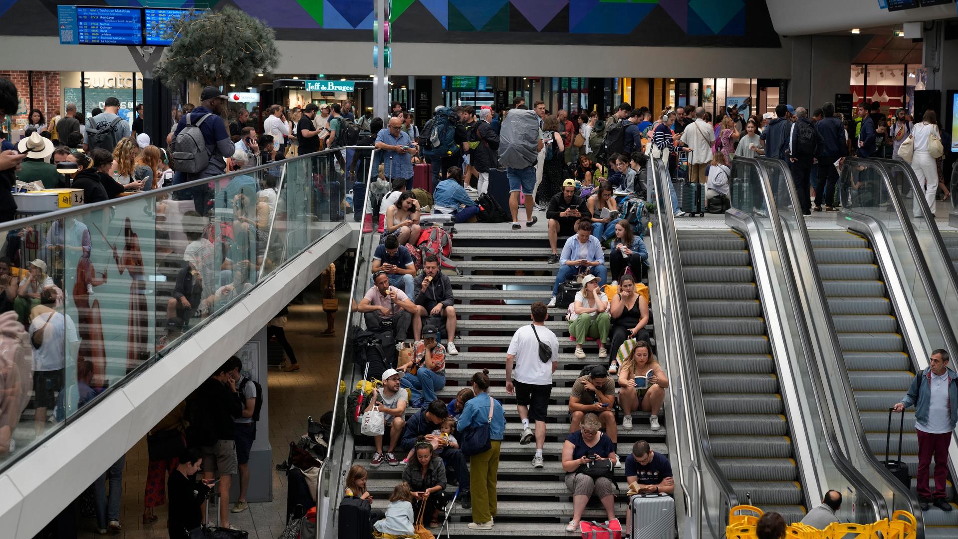 In dem Bahnhof Montparnasse in der französischen Haupt-Stadt Paris sitzen viele Reisende auf einer Treppe.