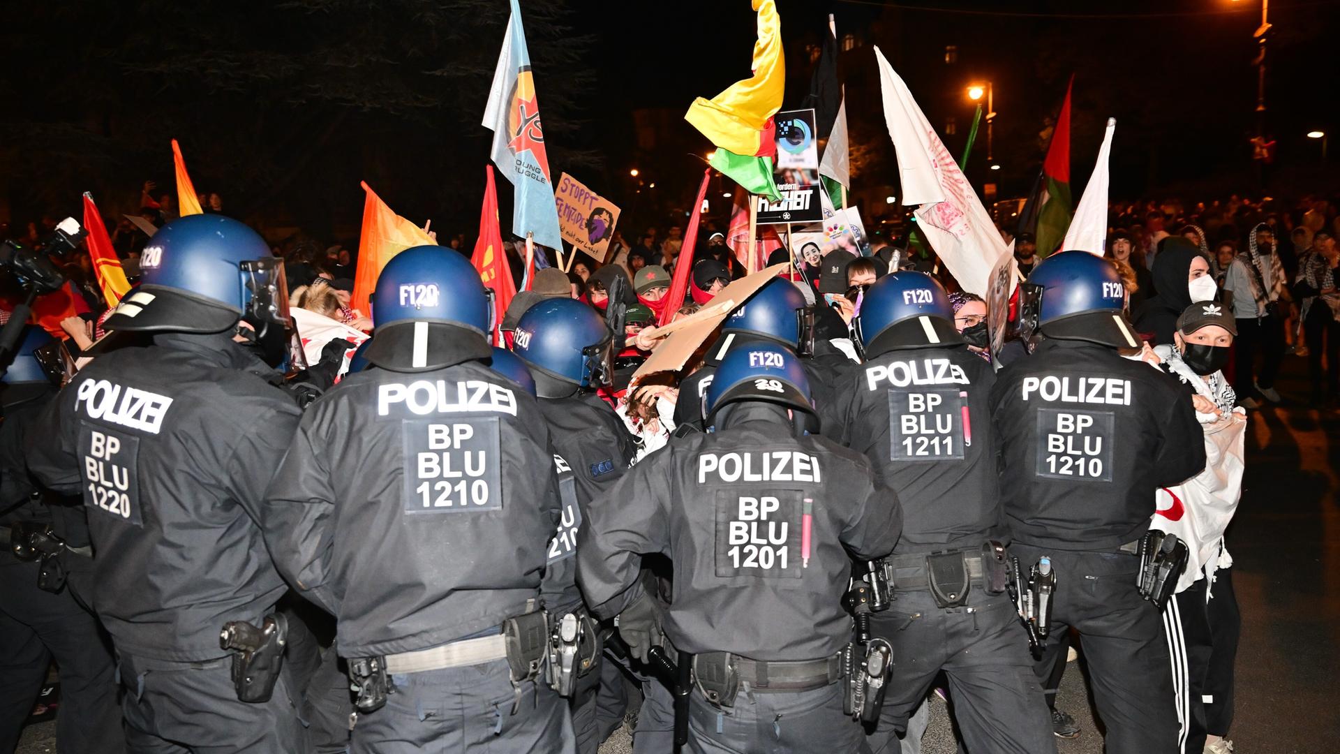 Polizeibeamte drängen teils vermummte Demonstranten mit Fahnen und Bannern zurück