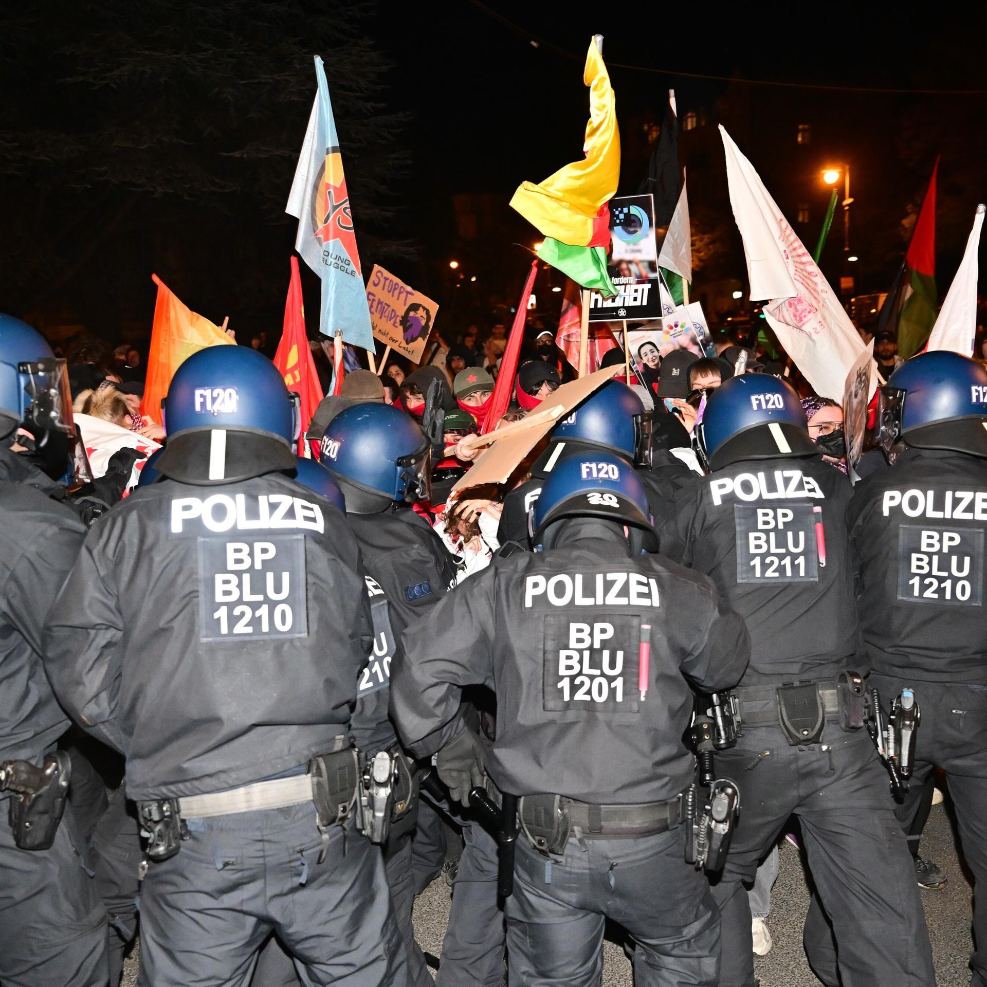 Polizeibeamte drängen teils vermummte Demonstranten mit Fahnen und Bannern zurück