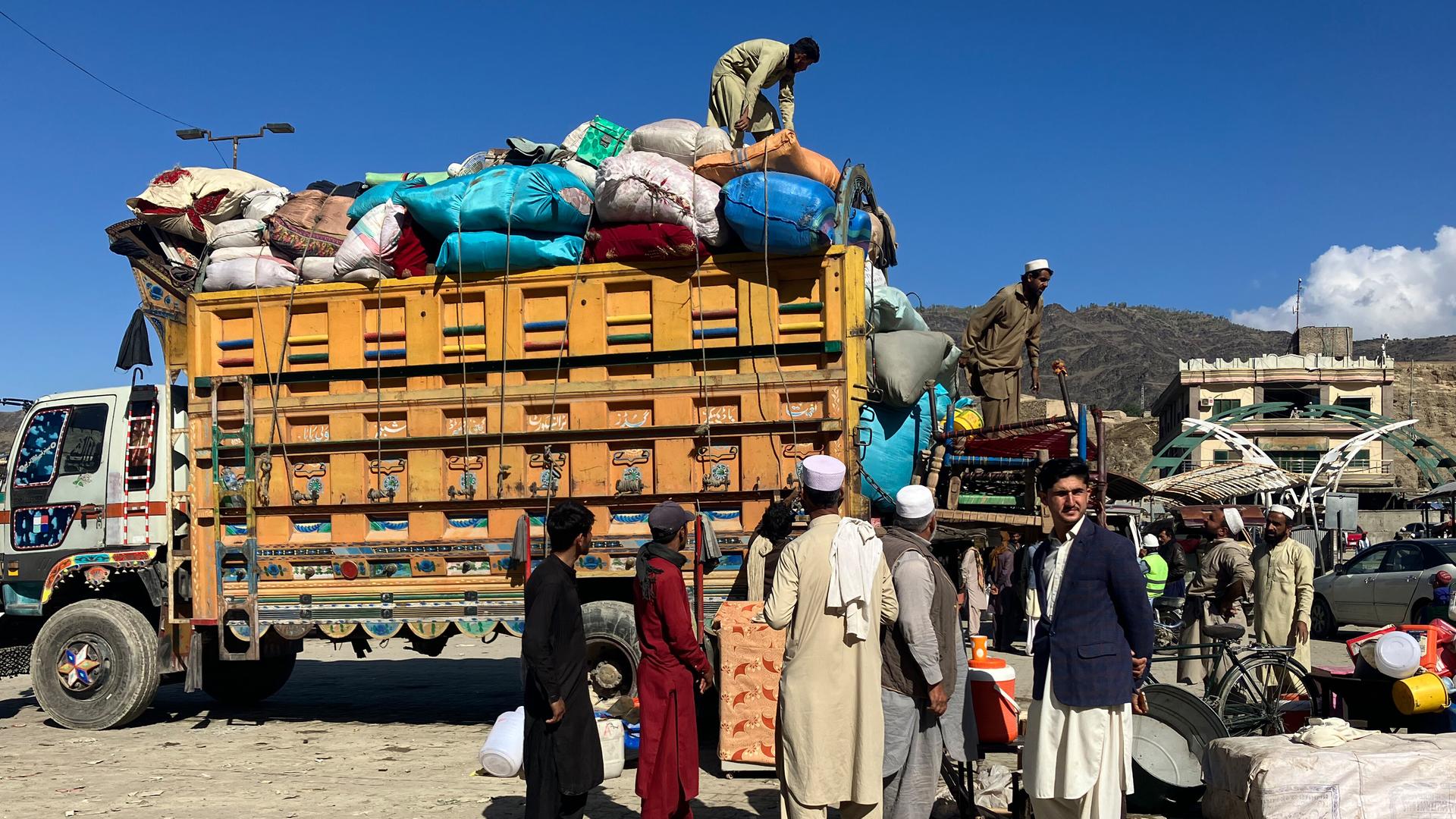 Afghanen vor einem Lkw, der mit Säcken und Gepäck beladen ist Afghanen vor einem Lkw, der mit Säcken und Gepäck beladen ist