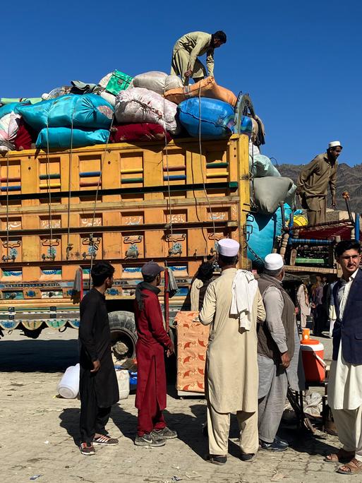 Afghanen vor einem Lkw, der mit Säcken und Gepäck beladen ist