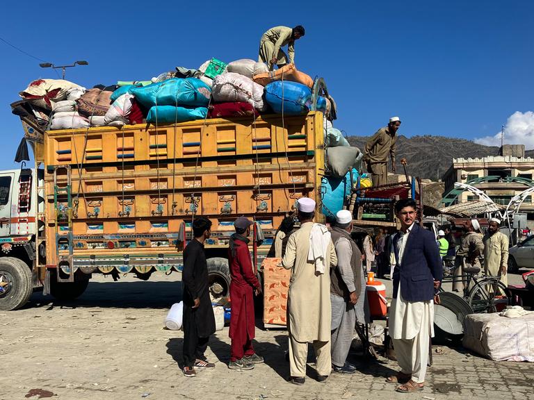 Afghanen vor einem Lkw, der mit Säcken und Gepäck beladen ist