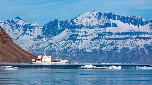 An der Nordostküste von Grönland fährt ein Eisbrecher mit Touristen an Bord an einem Fjord entlang.