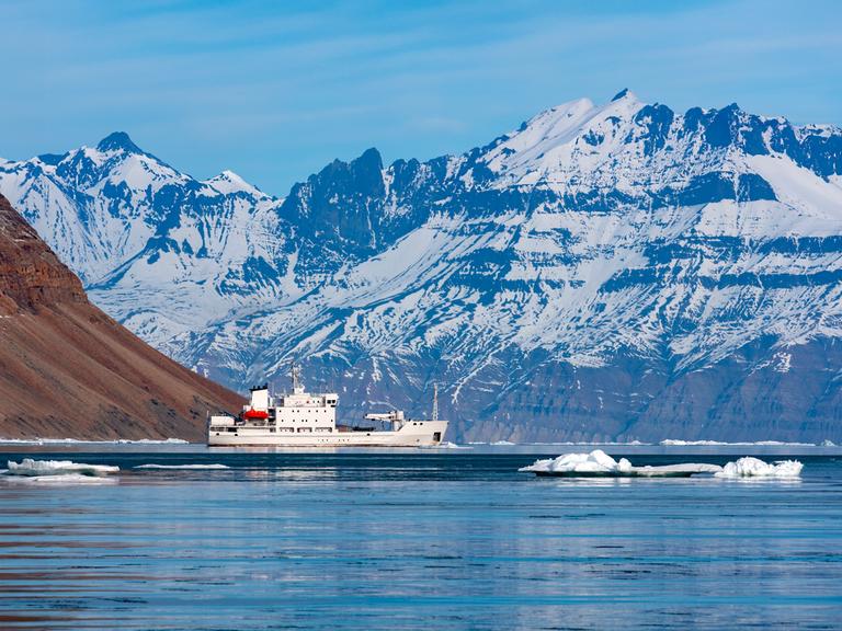 An der Nordostküste von Grönland fährt ein Eisbrecher mit Touristen an Bord an einem Fjord entlang.