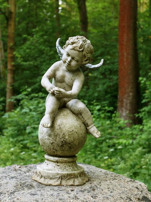 Ein kleiner sitzender Engel auf einem Friedhof.